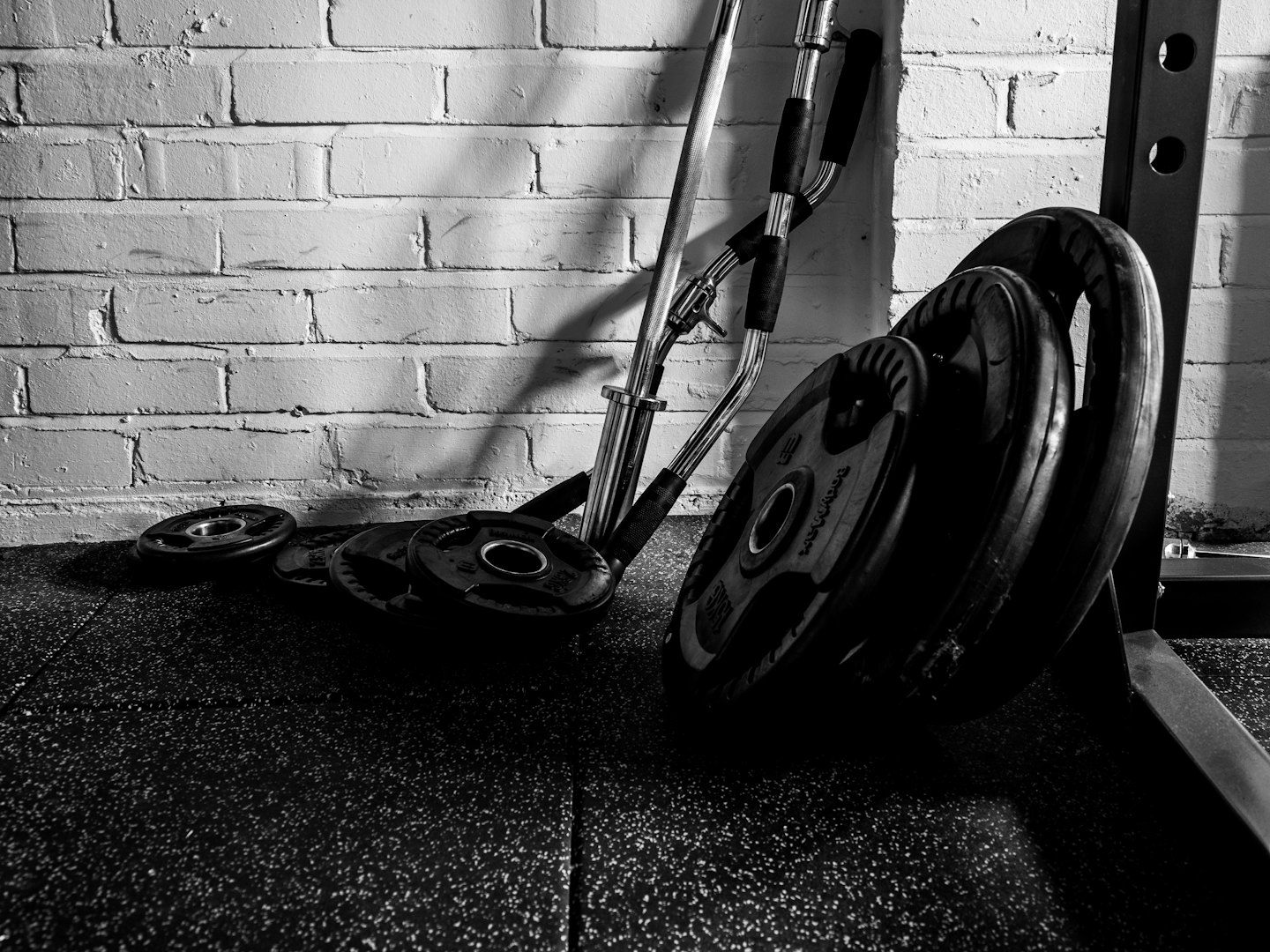 Metal barbells and weight plates leaning against a brick wall.